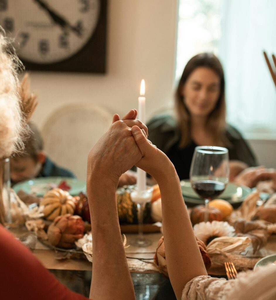 A family holding hands in prayer before a Thanksgiving dinner indoors with warm fall decor.
