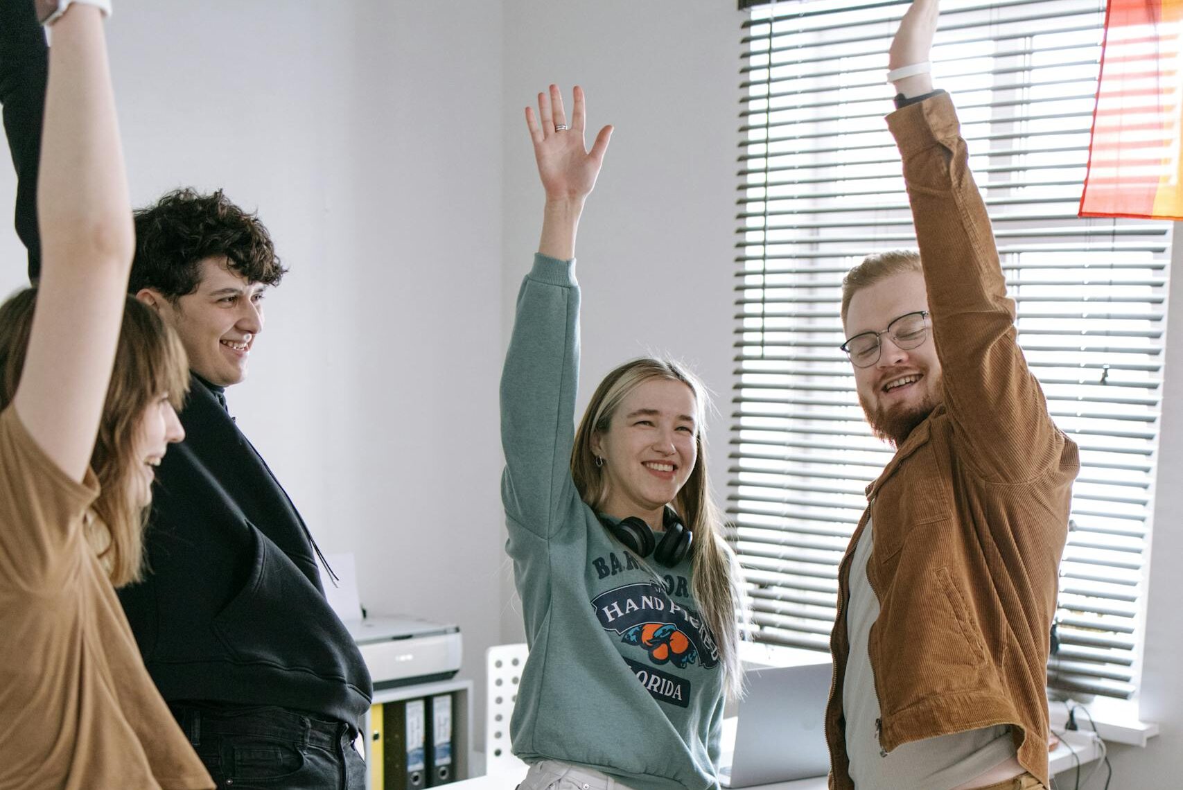 Un grupo alegre y diverso de jóvenes adultos celebrando en un espacio de oficina, encarnando el trabajo en equipo y el éxito.
