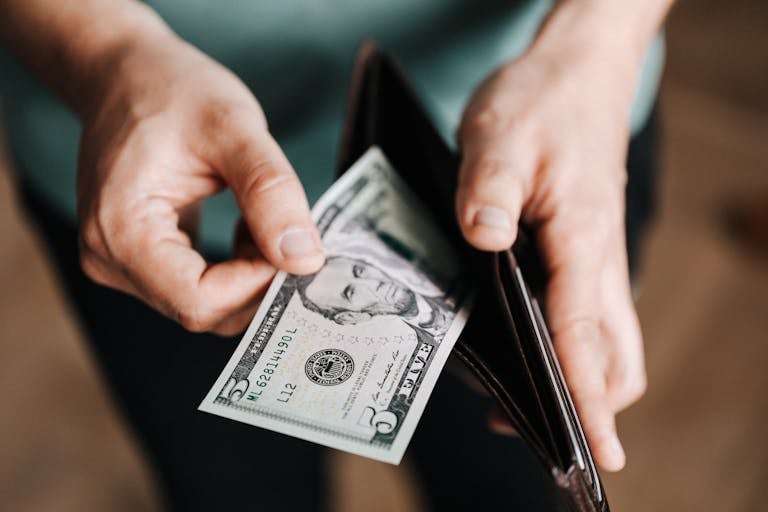 Una persona saca un billete de cinco dólares de una billetera, lo que simboliza un termostato financiero en abundancia.
