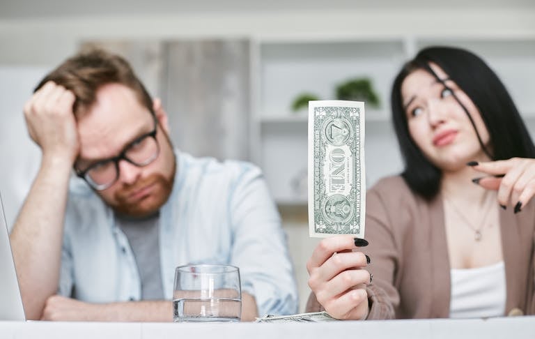Una pareja interracial adulta expresa preocupación por sus finanzas mientras sostienen un billete de un dólar en el interior.