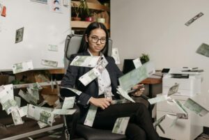 Mujer de negocios en una oficina moderna con dinero cayendo, simbolizando el éxito financiero y una mente millonaria.