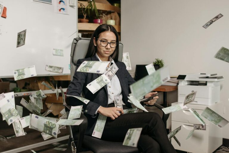 Mujer de negocios en una oficina moderna con dinero cayendo, simbolizando el éxito financiero y una mente millonaria.