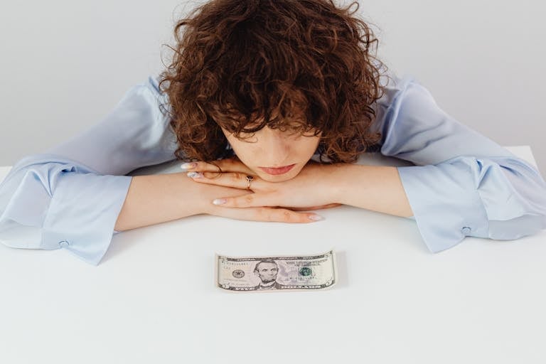 Mujer caucásica con cabello rizado reflexionando sobre las mentiras sobre el dinero con un billete de cinco dólares.