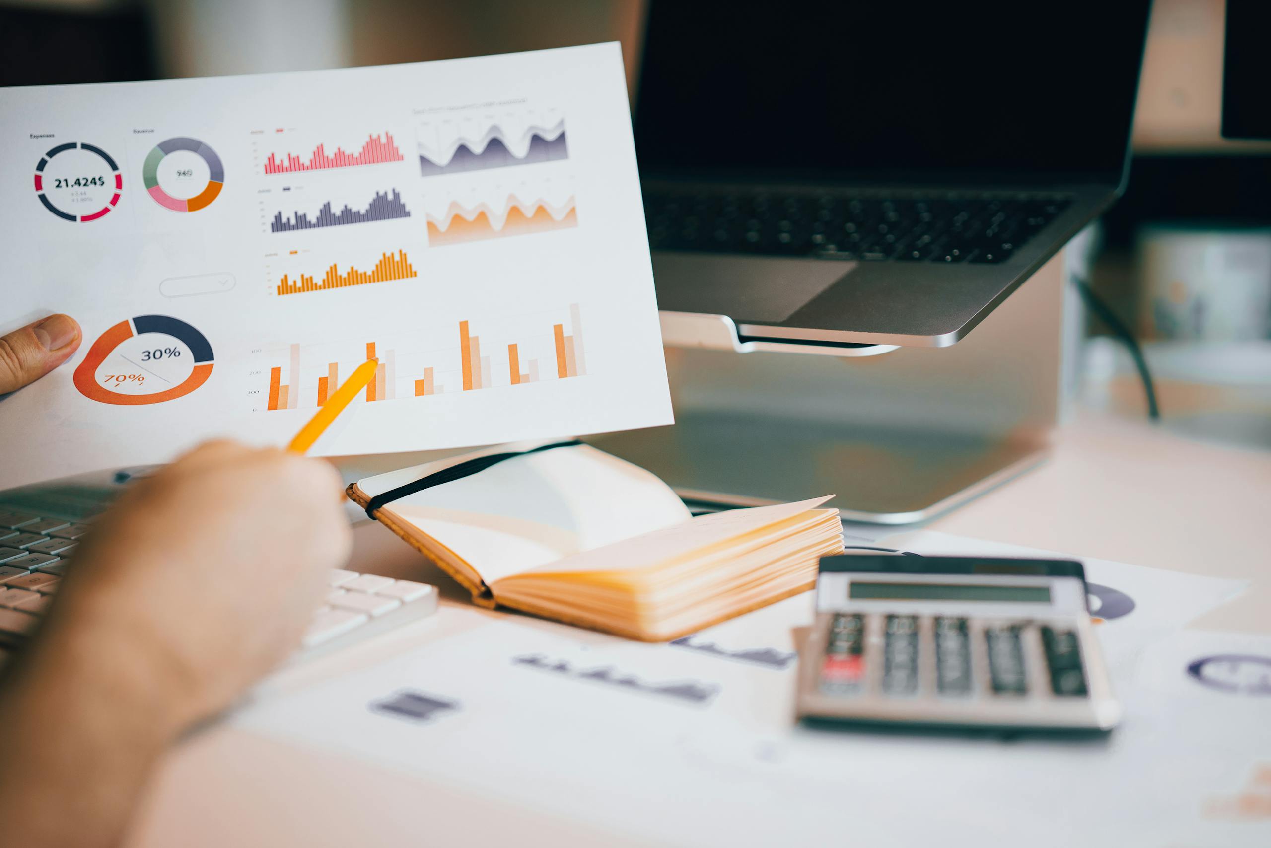 Primer plano de manos analizando datos financieros con gráficos, computadora portátil y calculadora.