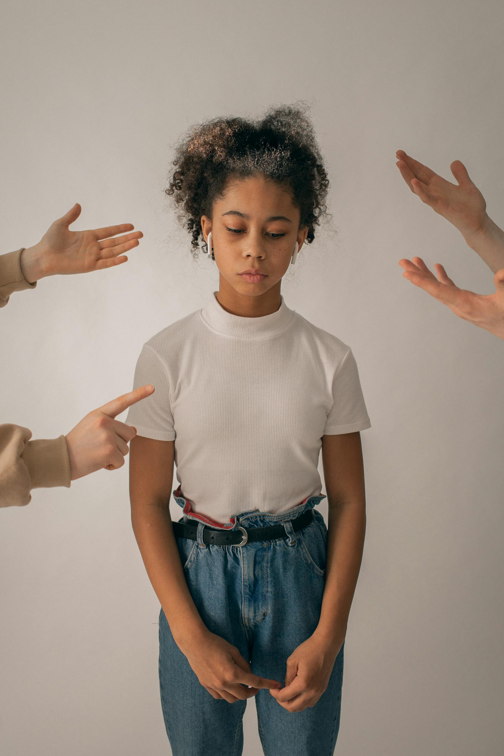 Personas regañan a una adolescente afroamericana decepcionada con ropa informal de pie sobre un fondo blanco con cara triste en el estudio.