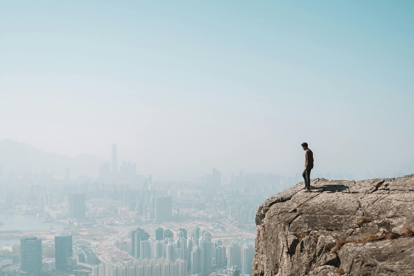 Un hombre se encuentra en un acantilado con vistas al impresionante horizonte de Hong Kong, capturando la mezcla de entornos urbanos y naturales simbolizando la grandeza respecto a los problemas.
