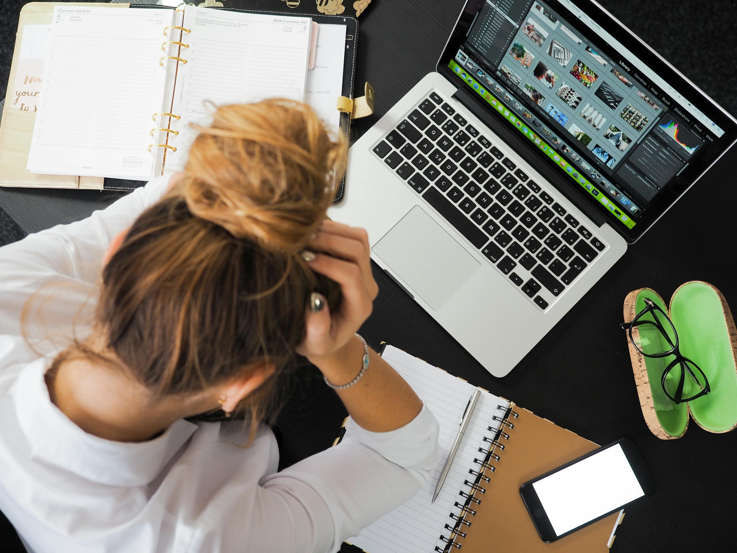 Vista aérea de una mujer estresada al reprogramar su relación con el dinero que trabaja en un escritorio con una computadora portátil, un teléfono y cuadernos.