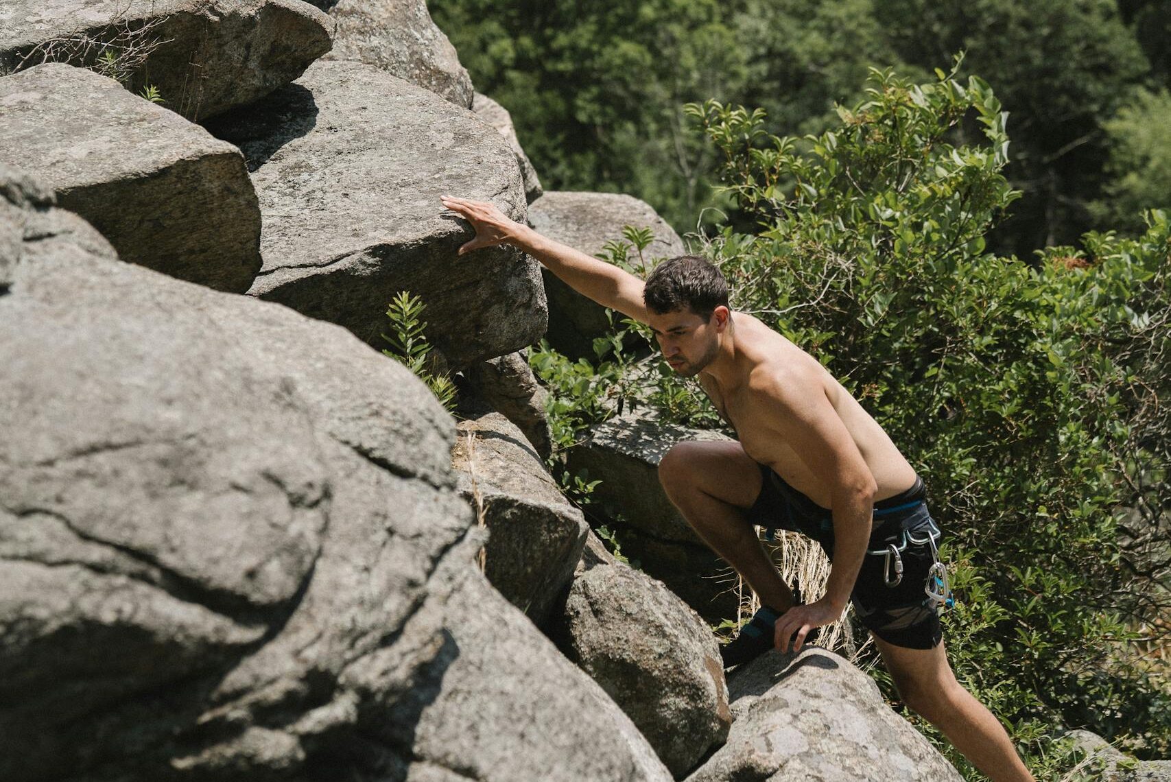 Hombre sin camisa escalando un terreno rocoso al aire libre mostrando determinación, fuerza y resiliencia.