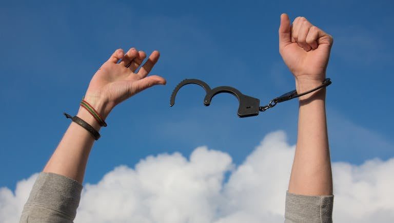 Imagen simbólica de la libertad de creencias limitantes con las esposas abiertas contra un cielo azul brillante.