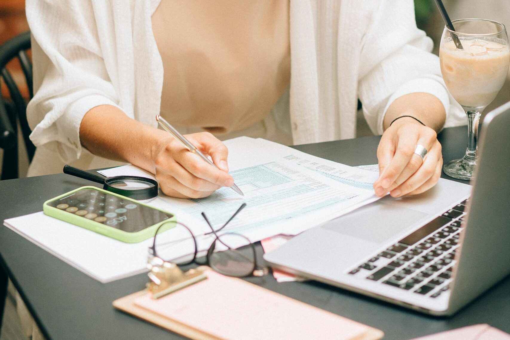 Mujer analizando documentos financieros usando una computadora portátil y calculadora en el interior.