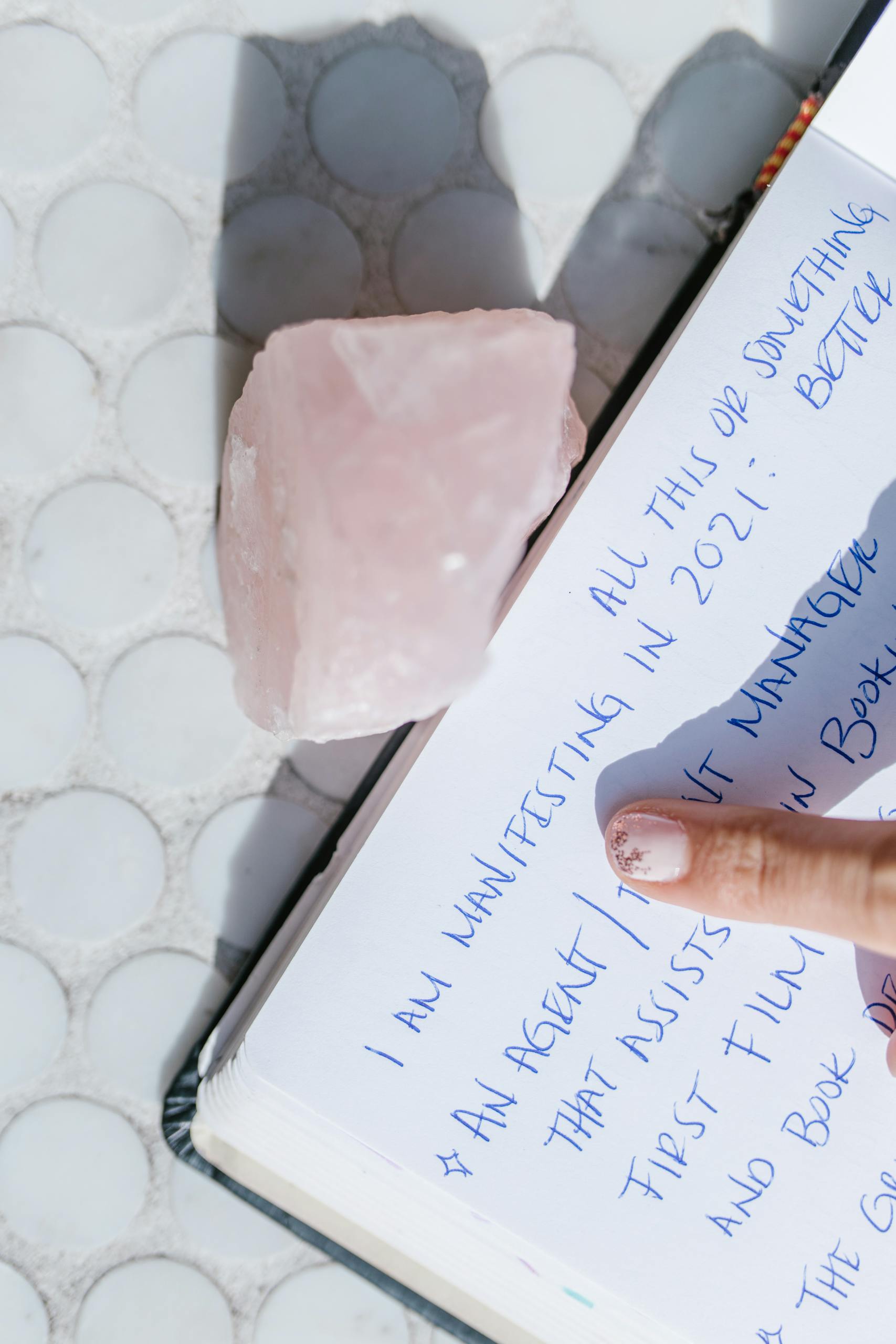 Primer plano de una página del diario de manifestación con un cristal de cuarzo rosa y un dedo señalando.