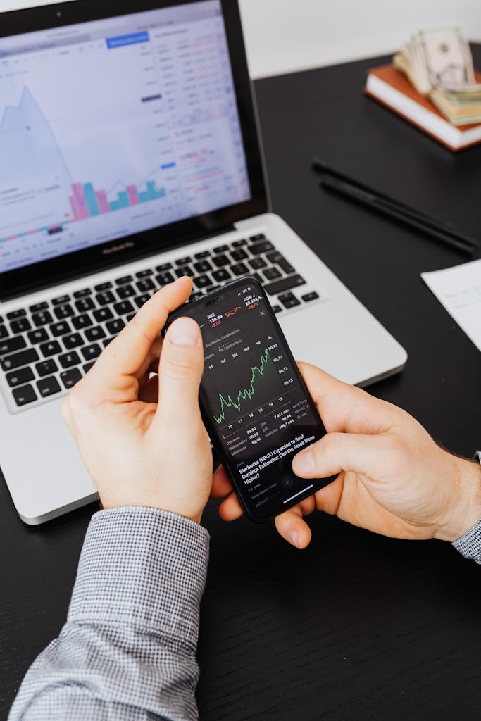 Primer plano de manos examinando gráficos del mercado de valores en un teléfono inteligente y una computadora portátil simbolizando un perfil de inversor agresivo.