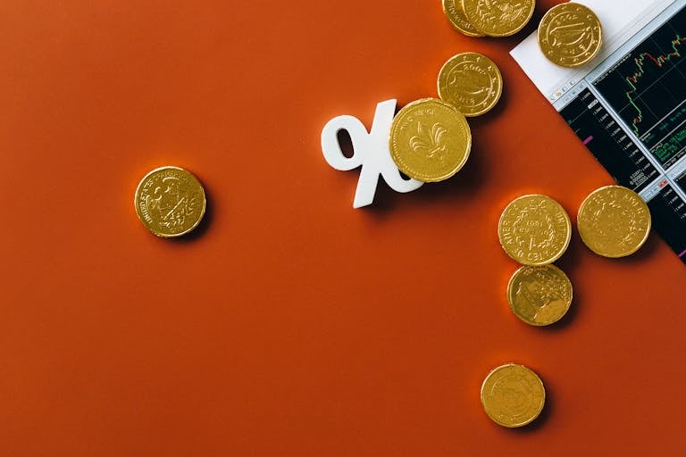 Monedas de oro esparcidas con un gráfico de mercado de valores y un símbolo de porcentaje sobre un fondo naranja simbolizando el cálculo de tasas de interés.