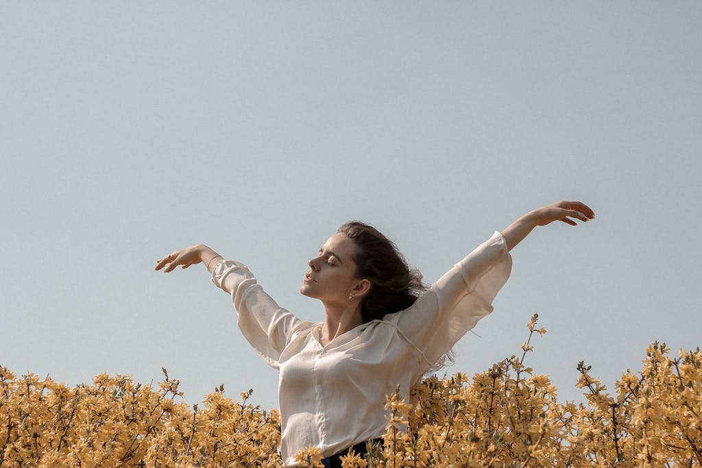 Mujer con los brazos levantados en un campo soleado de flores amarillas, simbolizando un perfil de inversor conservador.