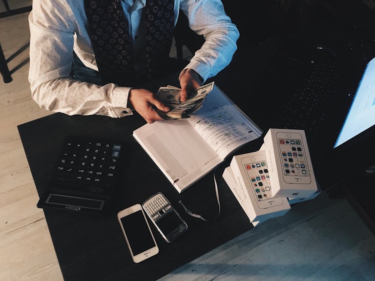 Empresario organizando sus finanzas con dispositivos tecnológicos y efectivo sobre el escritorio, representando como se relacionan la historia personal y decisiones financieras.