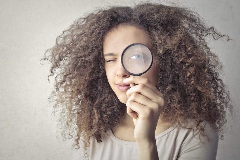 Retrato en primer plano de una mujer guiñando un ojo y sosteniendo una lupa sobre un fondo blanco, simbolizando qué mirar antes de firmar un préstamo.